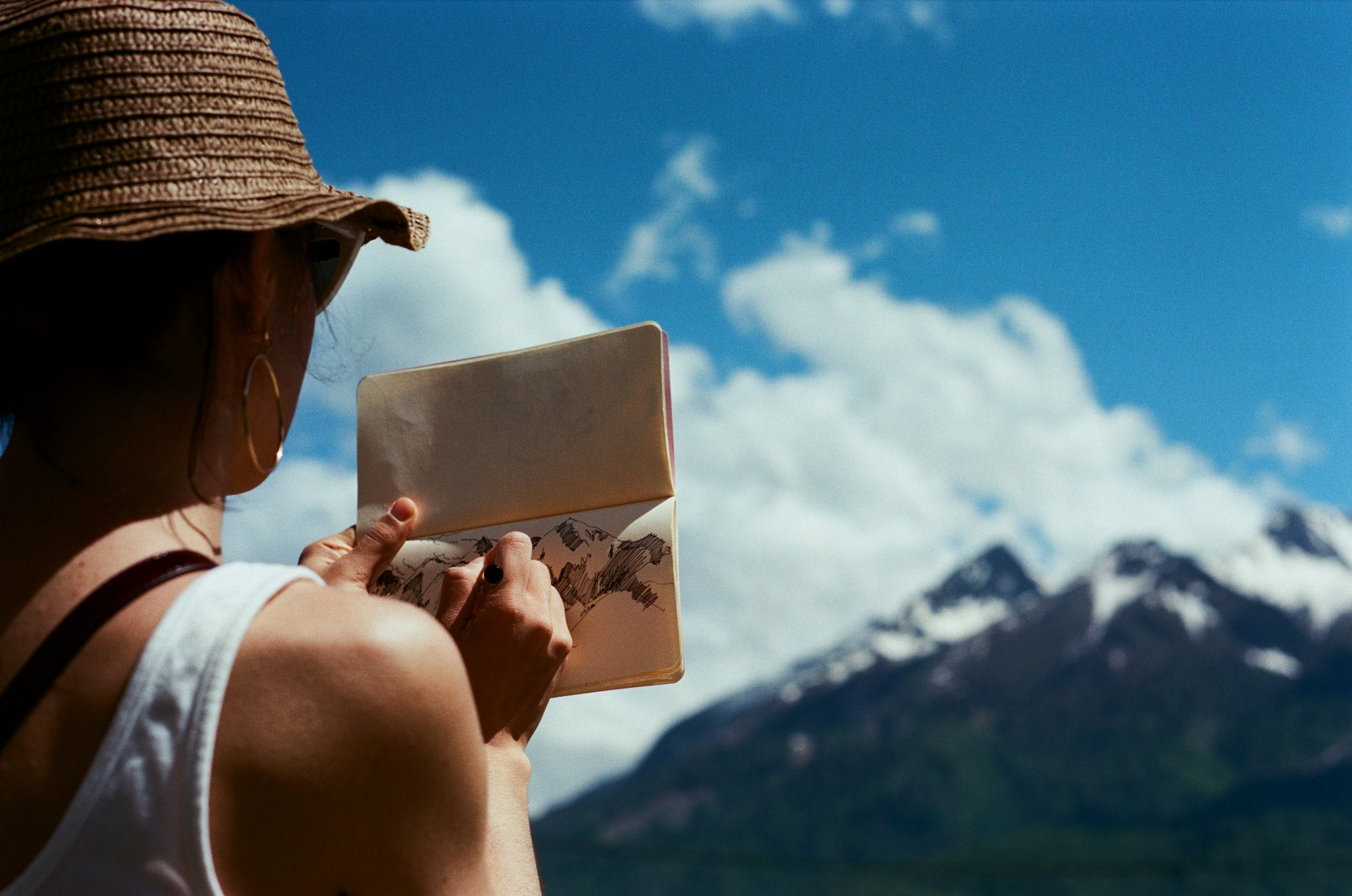 A traveler sketching mountains in a notebook — Carnets turns your travel memories into a beautiful journal