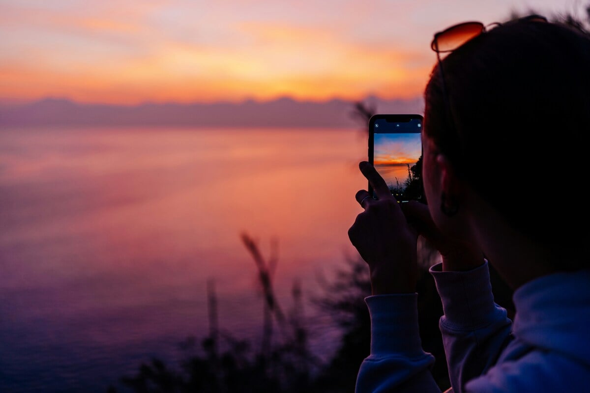 A woman taking a picture of a sunset with her cell phone
